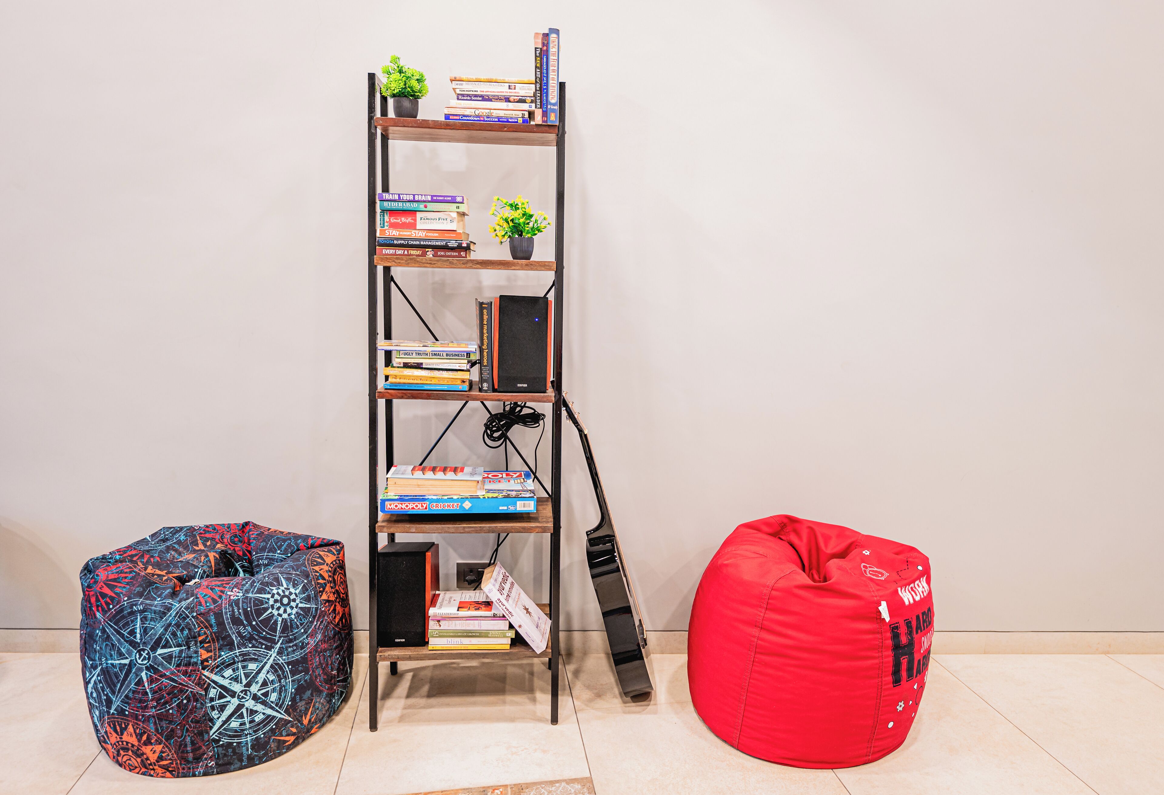 A bookshelf with books and small plants, two bean bags, and a black speaker.