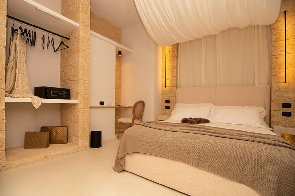 A bedroom with a large bed, a chair, a shelf with clothes, and a small table.