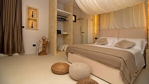 A bedroom with a large bed, a stone wall, a shower area, and a hanging light fixture. - Borgo Bevagna Relais (Manduria)