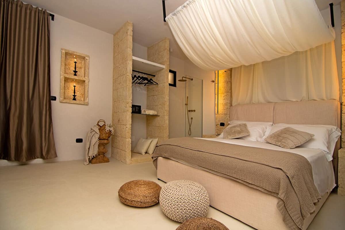 A bedroom with a large bed, a stone wall, a shower area, and a hanging light fixture.