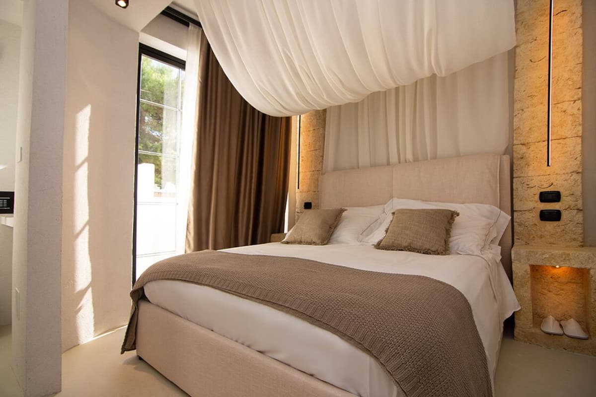 A modern bedroom with a large bed, beige bedding, and a stone accent wall.