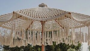 A round wooden table with two glasses of white wine, a white cloth, and a macrame umbrella. - Borgo Bevagna Relais (Manduria)