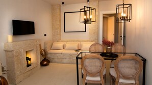 A modern living room with a stone fireplace, a sofa, a glass coffee table, wicker chairs, and a flat-screen TV mounted on the wall. - Borgo Bevagna Relais (Manduria)