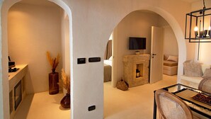 A modern living room with an arched doorway, a fireplace, a flat-screen TV, and a dining area with a glass table and wicker chairs. - Borgo Bevagna Relais (Manduria)