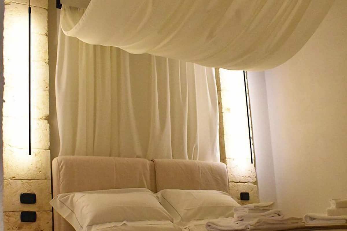 A bed with a canopy, white linens, and a brown throw blanket.