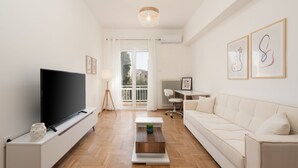 A modern living room with a flat-screen TV, a sofa, a coffee table, and a desk with a chair.