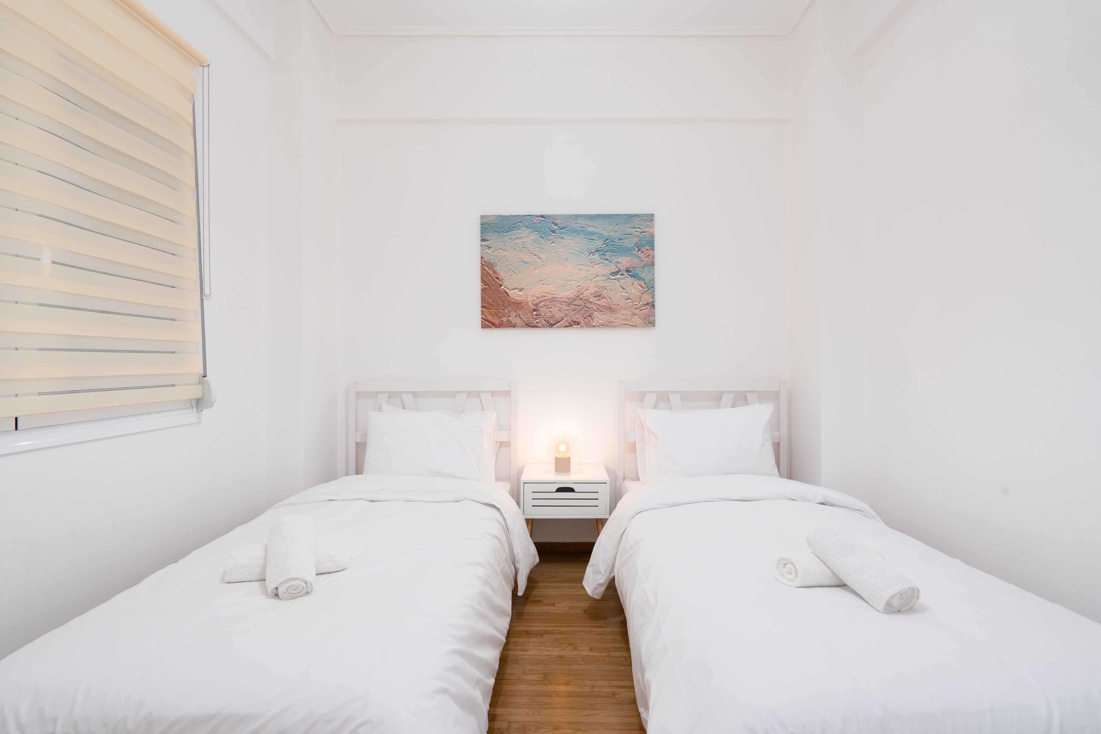 A room with two beds, a nightstand with a lamp, and a painting on the wall.