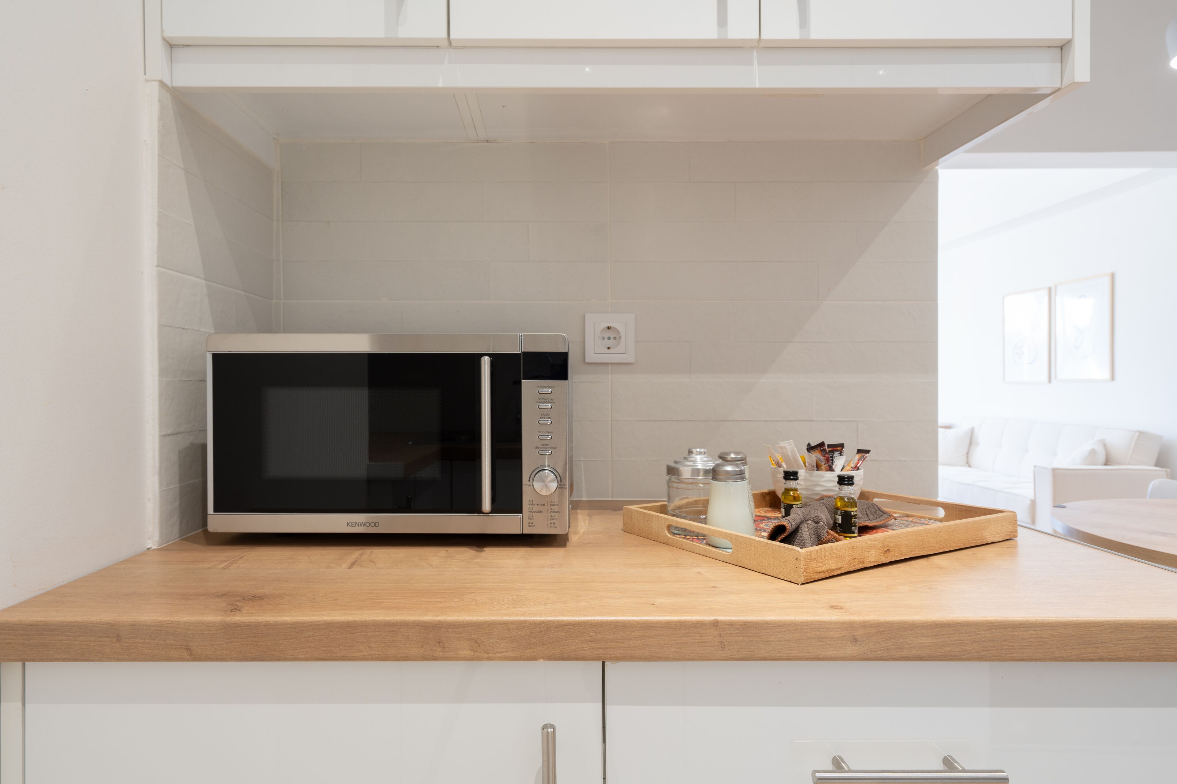 Una cocina con microondas, encimera de madera y una bandeja con utensilios de cocina.