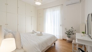 A bedroom with a bed, bedside table, lamp, wardrobe, potted plant, and an air conditioning unit.