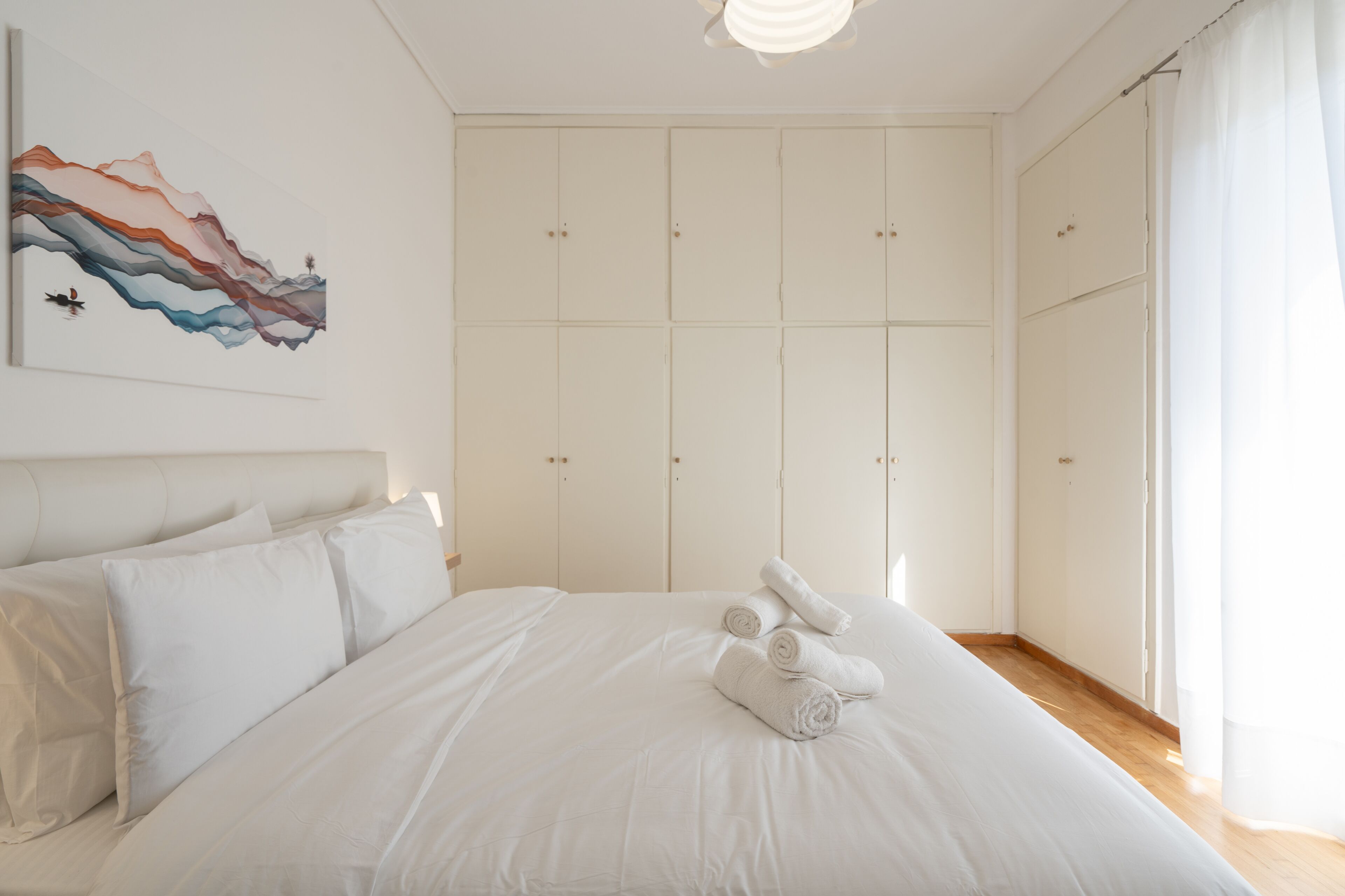Une chambre à coucher avec un grand lit, du linge de lit blanc, une tête de lit et une armoire à plusieurs portes.