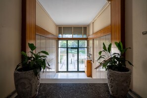 A hallway with a glass door leading outside, flanked by two large potted plants. - City Chic Apartment with Park View (Athens)