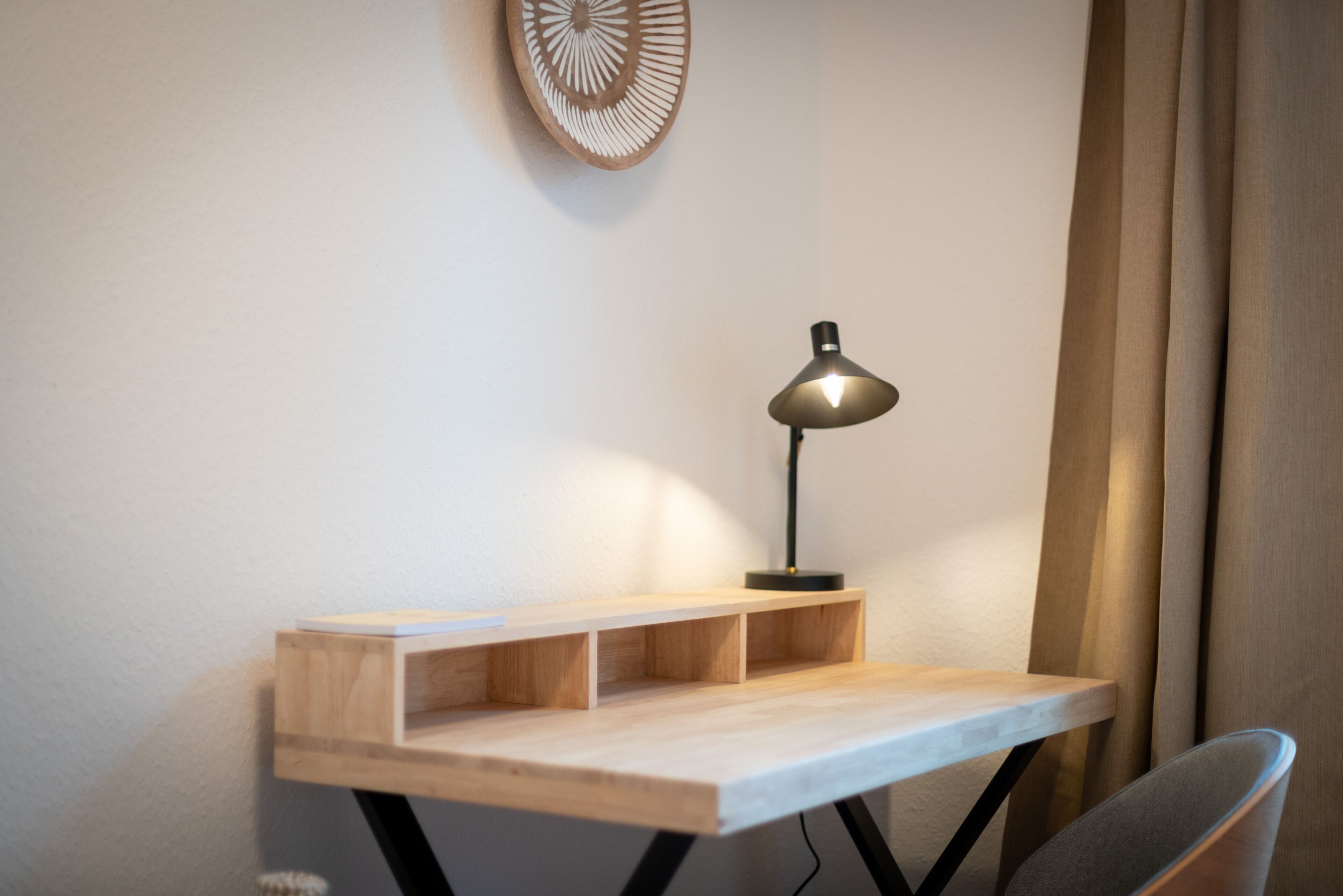 A desk with a lamp, a chair, and a wall-mounted decorative piece.