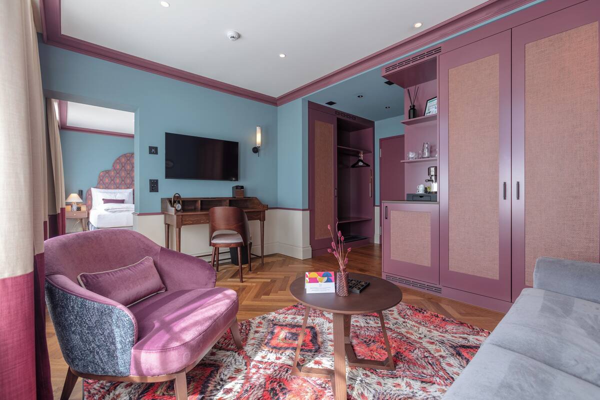 Une chambre d’hôtel moderne dotée d’un grand lit, d’un coin salon avec un canapé et un fauteuil, d’une petite table et d’une armoire.