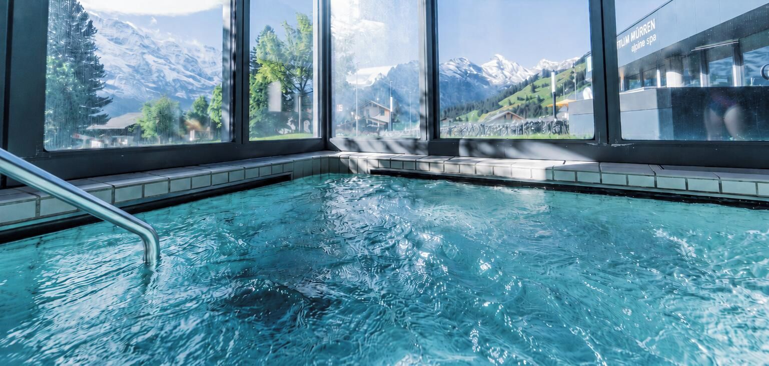 Piscina com vista para montanhas nevadas através de grandes janelas.