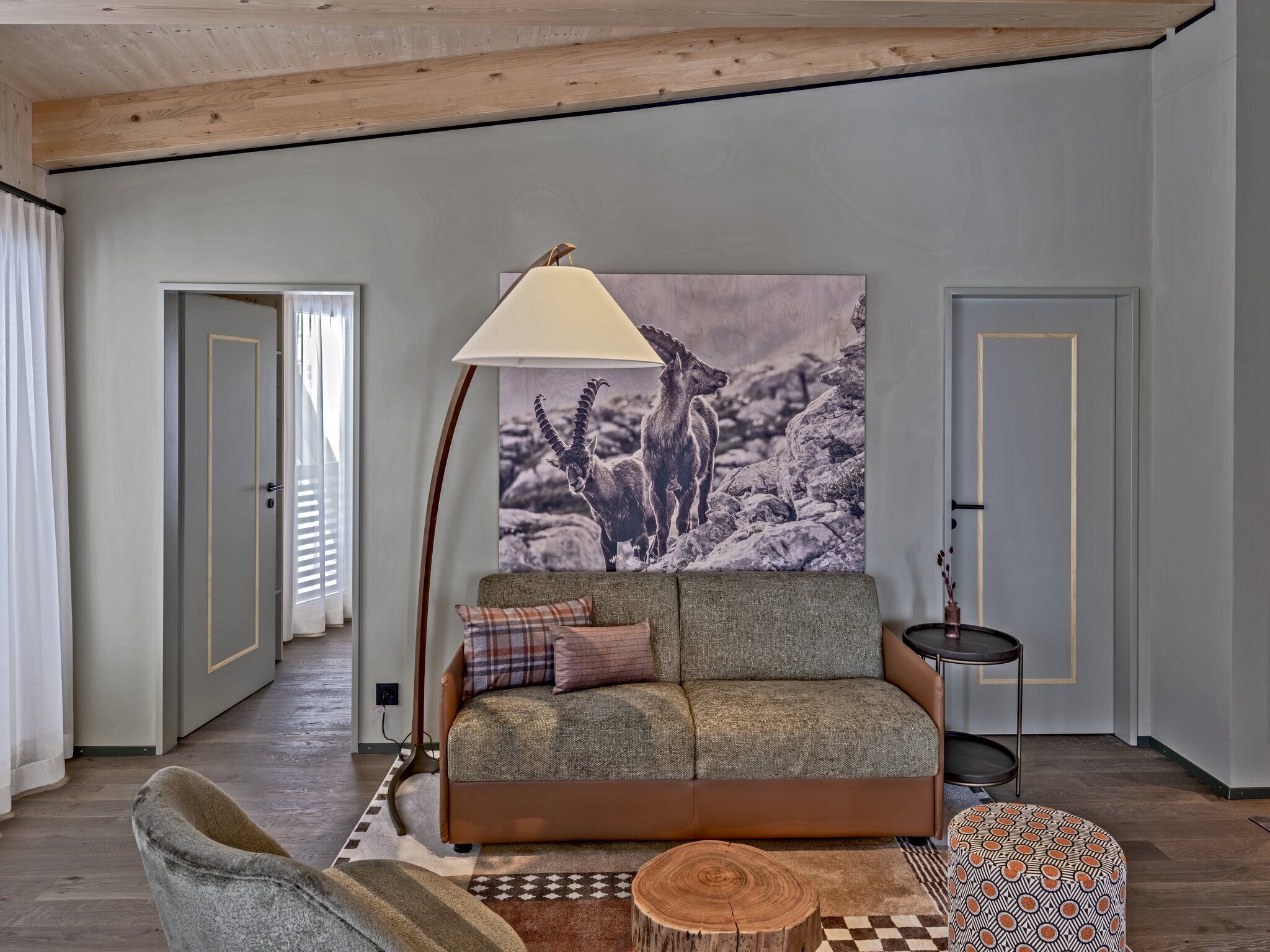 Un salon chaleureux avec un canapé, une lampe et une grande œuvre d’art murale représentant un paysage de montagne.