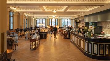 A spacious hotel lobby with a bar area, wooden flooring, and large windows.