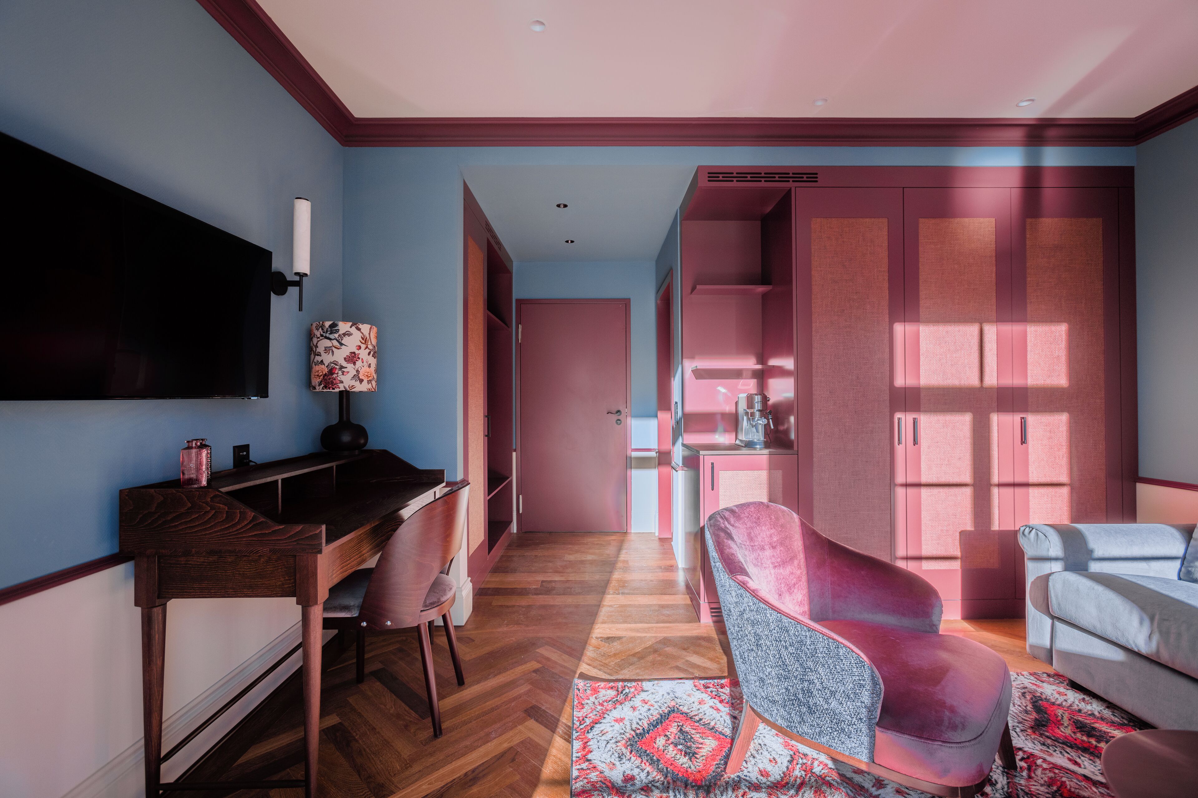 Una sala de estar moderna con un escritorio de madera, un sofá rosa y un sillón gris.