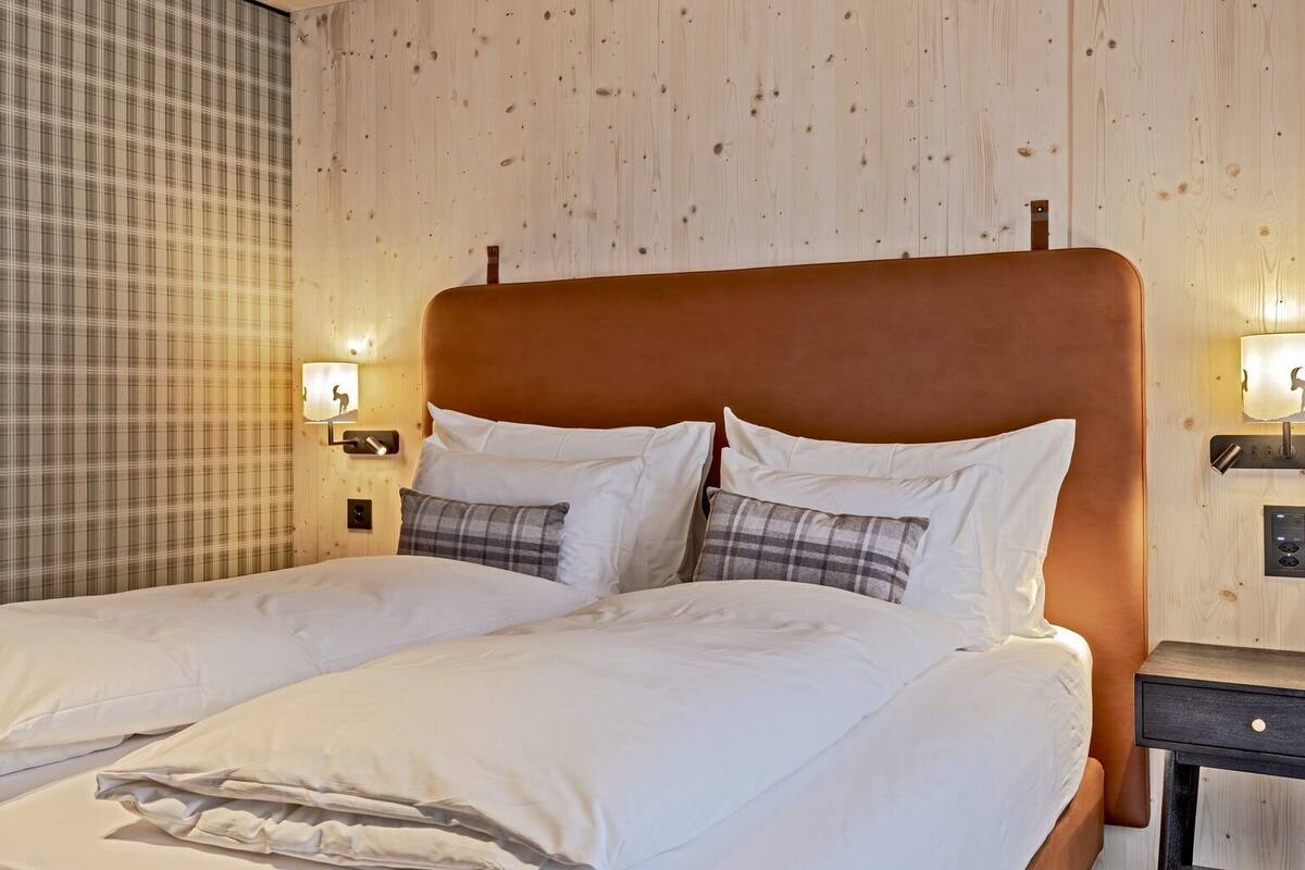 Un lit bien fait, avec du linge de lit blanc et des coussins à carreaux, une tête de lit en bois et une table de chevet avec une lampe.