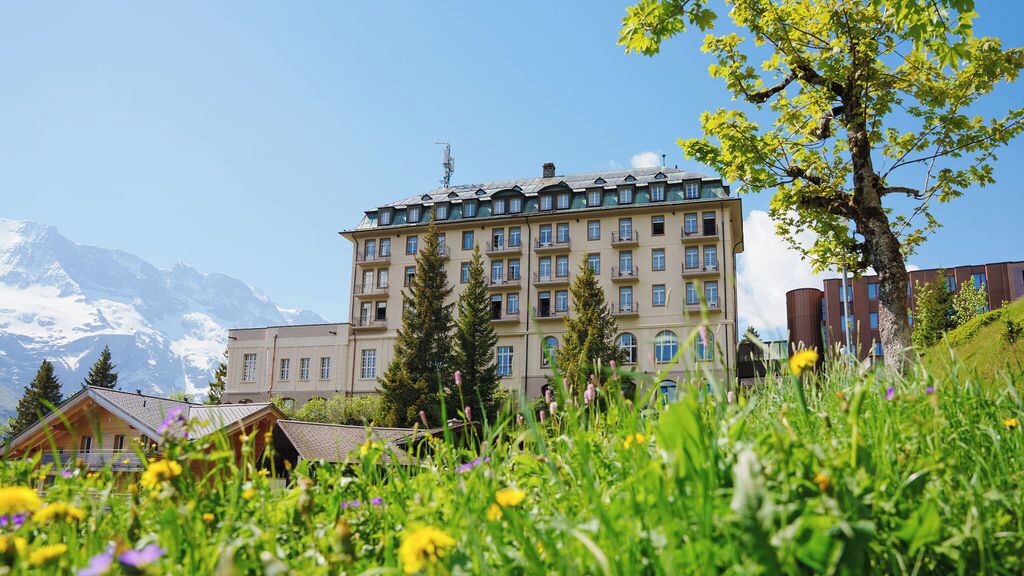 A multi-story hotel with a traditional architectural style, surrounded by lush greenery and mountains in the background.