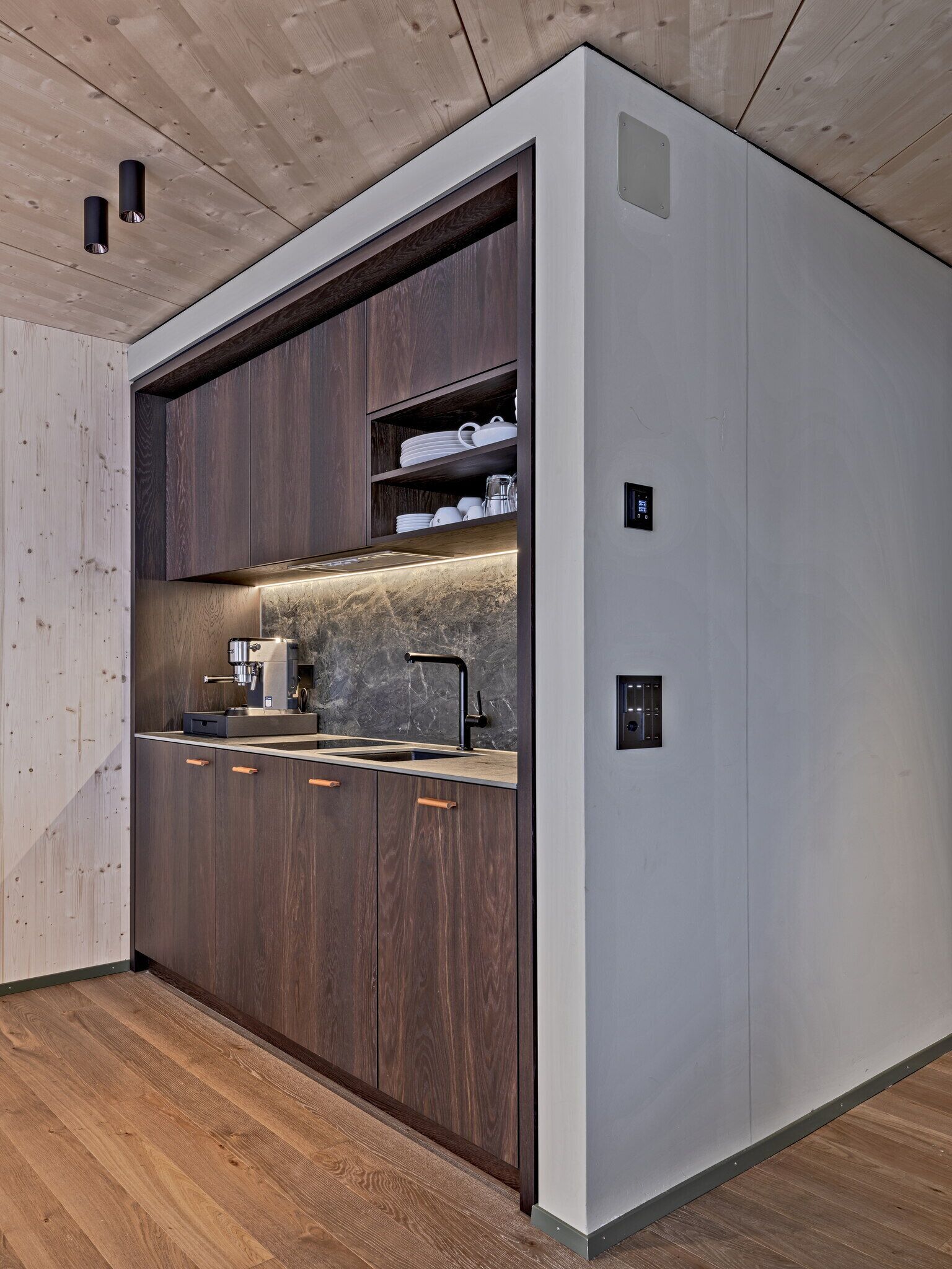 A modern kitchen with dark wood cabinets, a marble countertop, and a built-in coffee machine.