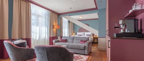 A modern living room with a grey sofa, two armchairs, a coffee machine, and a staircase leading to another level.
