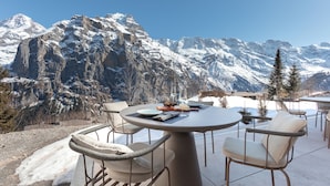 Un coin repas avec une table ronde et des chaises, le tout mis en valeur par un paysage de montagnes enneigées en arrière-plan.