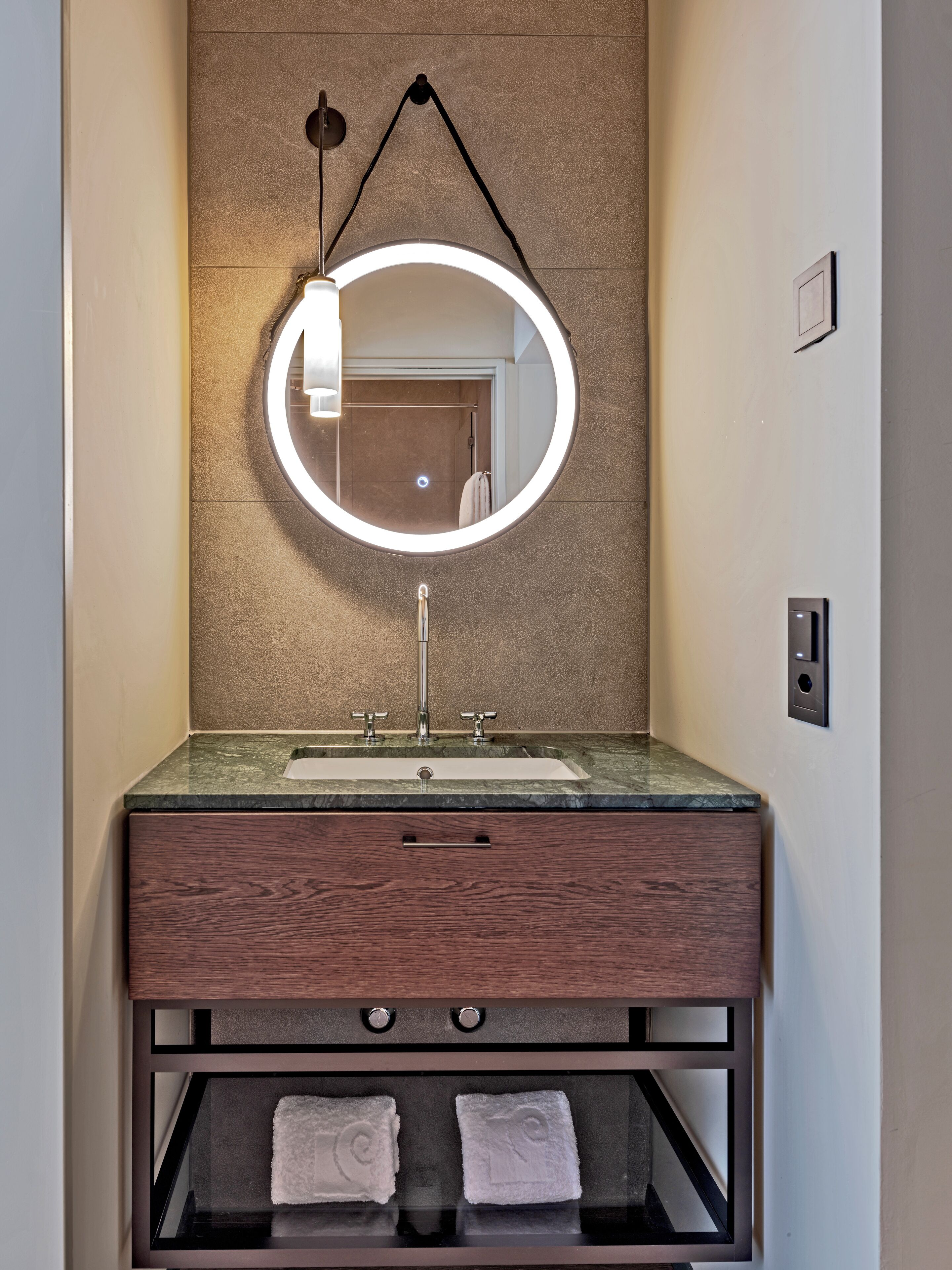 A bathroom vanity with a round mirror, a sink, and a towel rack.