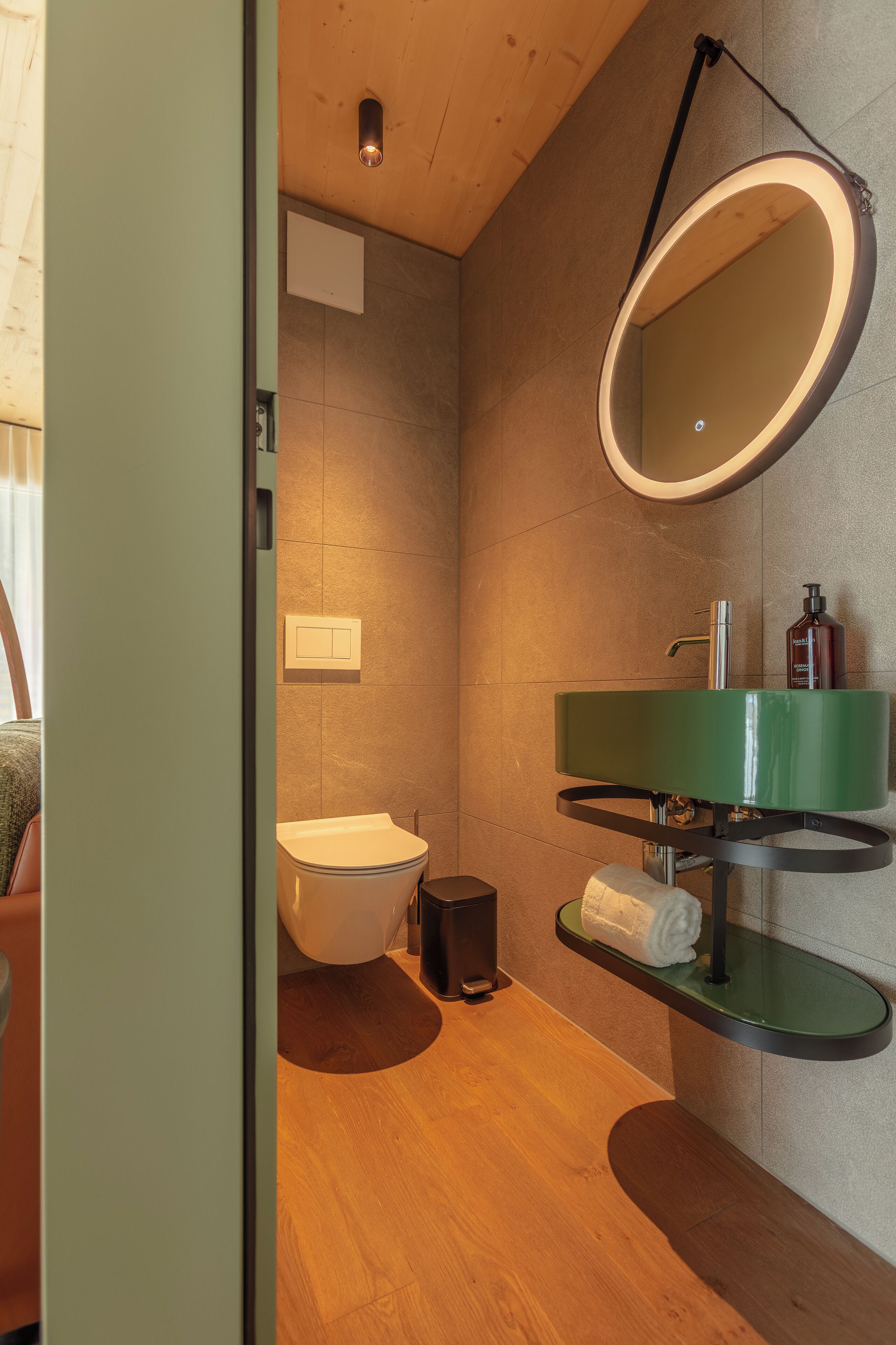 Ein modernes Badezimmer mit einem grünen Waschbecken, einem runden Spiegel und einer Toilette.