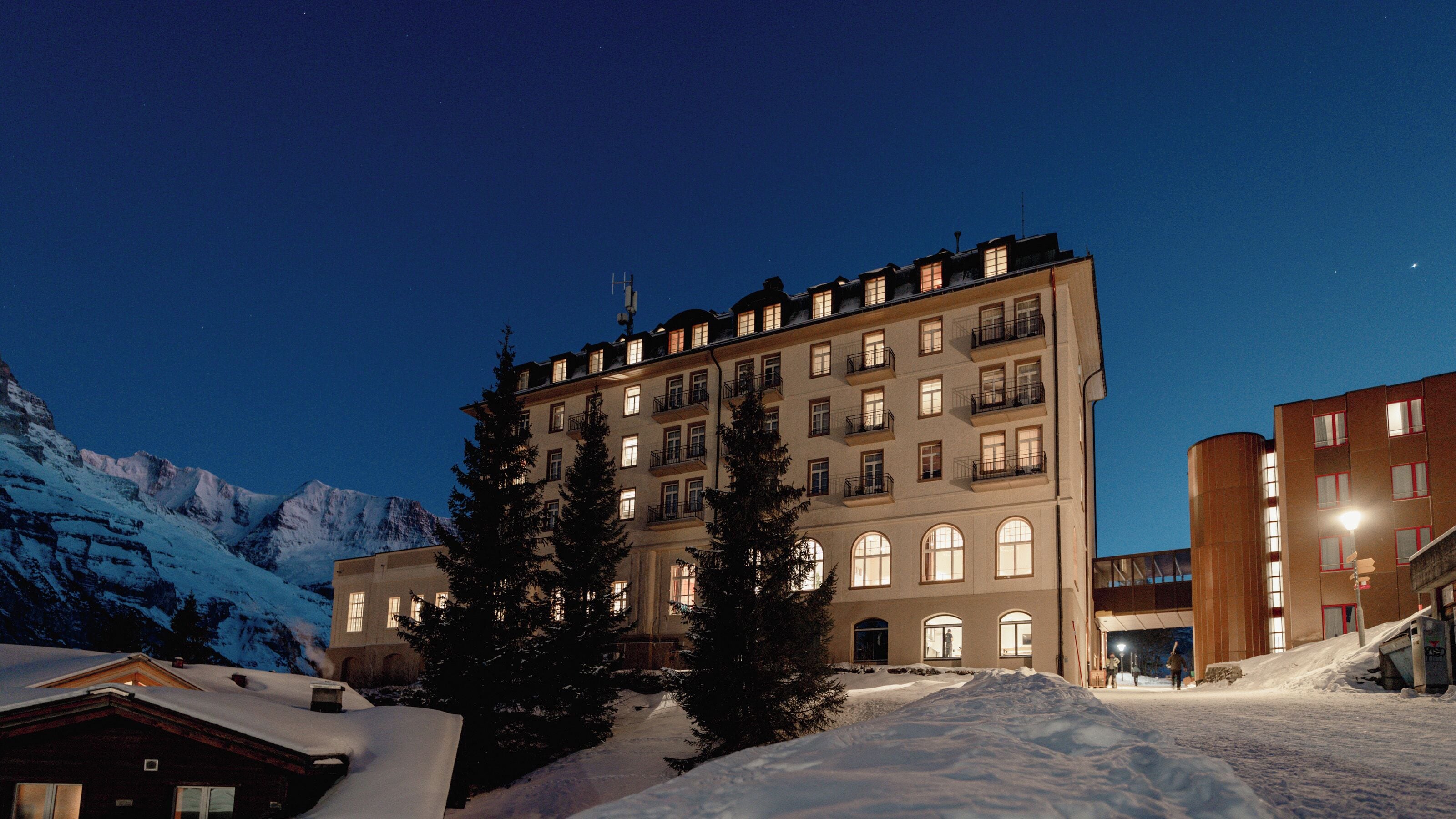 A multi-story hotel with a snow-covered landscape and mountains in the background.
