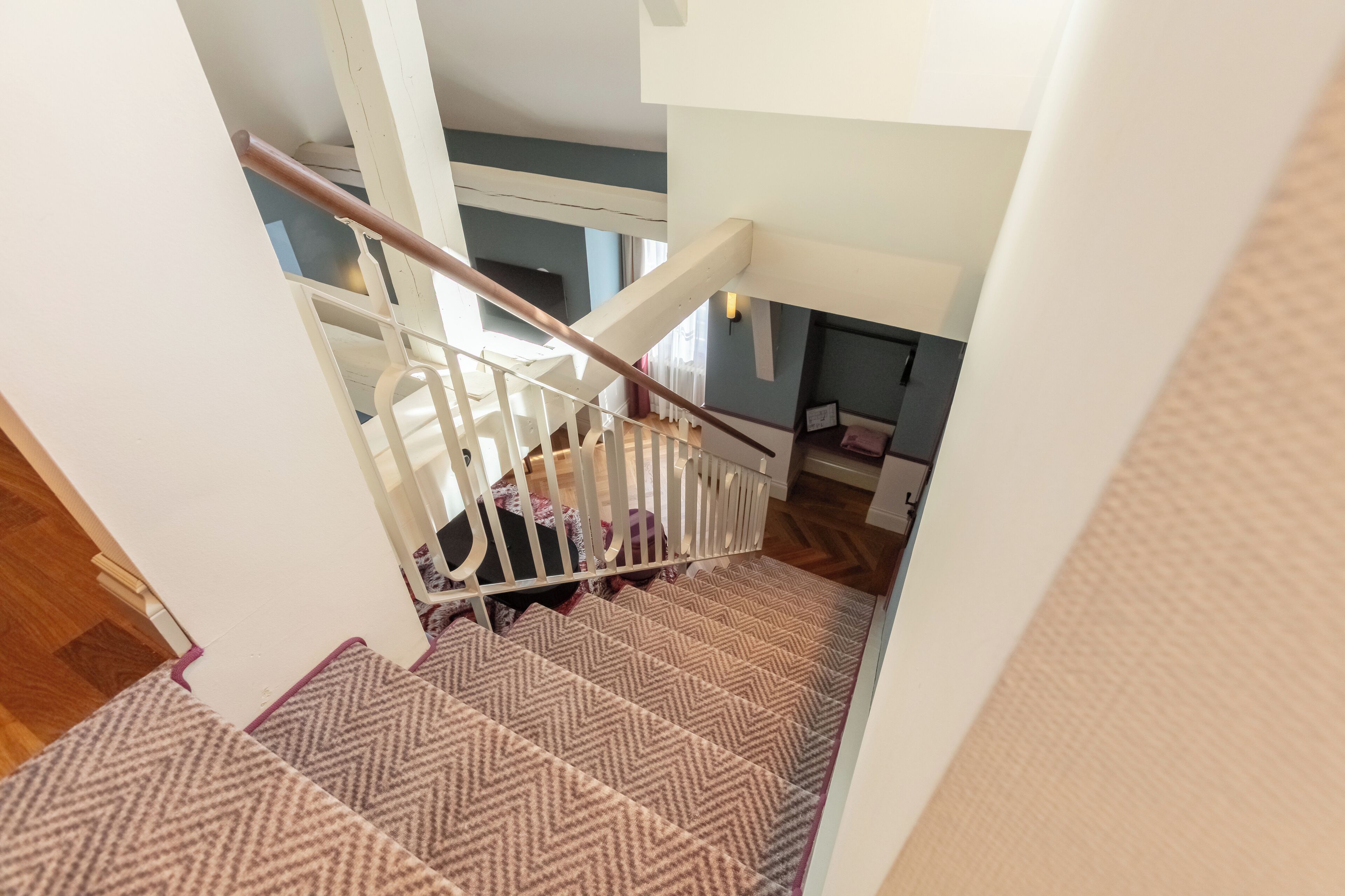 A staircase with a patterned carpet, white railings, and a wooden handrail.