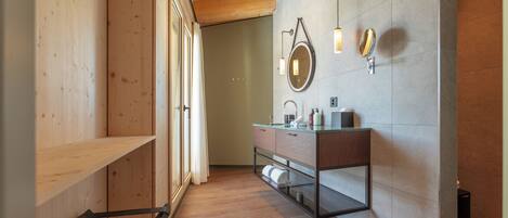 A modern bathroom with wooden flooring, a glass vanity, and a large mirror.
