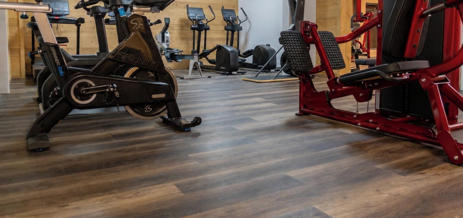 Een sportschool met diverse trainingsapparaten, waaronder een spinningfiets en een rode leg press machine.