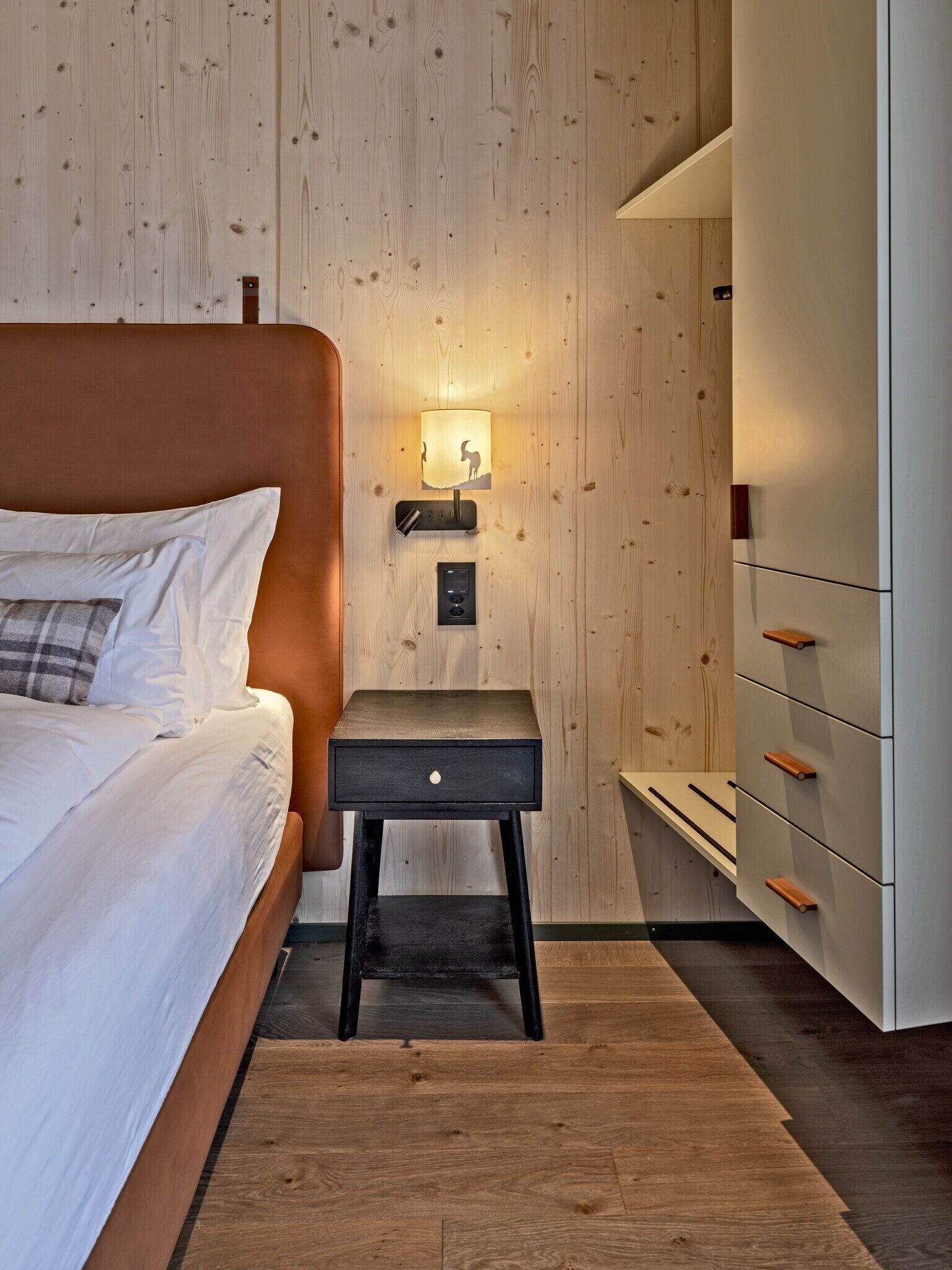 A bedroom with a bed, a nightstand, a lamp, and a dresser.