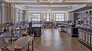 Un hall d’hôtel spacieux avec un long comptoir d’accueil, plusieurs espaces salon et un bar.