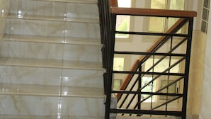 A marble staircase with a wooden handrail and black metal balusters, leading to an upper floor.