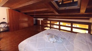 Un dormitorio con techo de madera, un tragaluz, una cama con colcha blanca y un armario de madera.