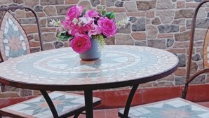 Una mesa redonda con una cubierta de mosaicos, rodeada de sillas con estructura y respaldo de metal.