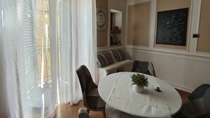 Un comedor con una mesa redonda, sillas, una planta en maceta y vistas al exterior a través de una ventana con cortinas.
