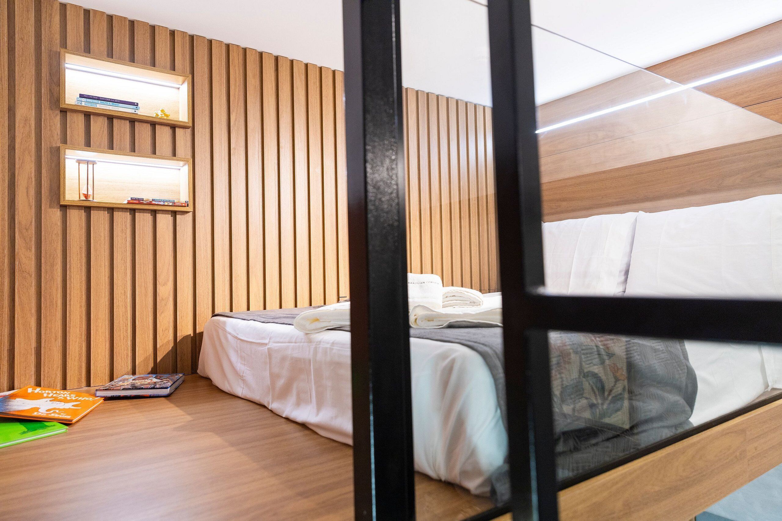 A modern bedroom with a bunk bed, wooden panel walls, and built-in shelves with books and decorative items.