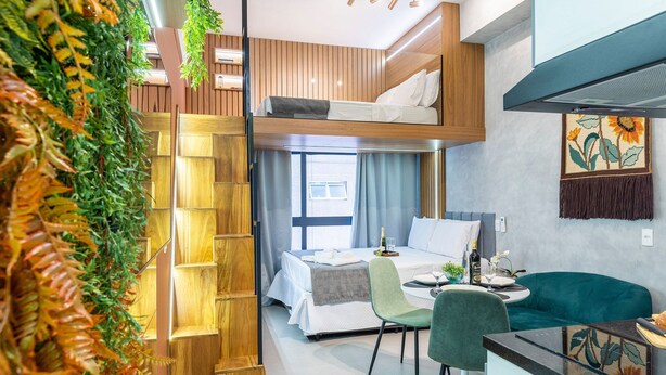 Une chambre d’hôtel moderne équipée d’un lit superposé, d’un coin repas avec une table et des chaises, et d’une grande fenêtre laissant entrer la lumière naturelle.