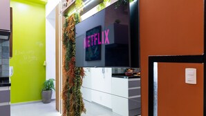 Une cuisine moderne dotée d’un grand téléviseur à écran plat affichant le logo de Netflix, d’un mur d’accent vert et d’une plante décorative.
