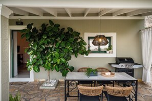 A patio with a table, chairs, a grill, and a potted plant.