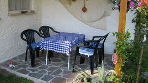 Un patio con mesa y sillas, suelo de piedra, una ventana y una hamaca colgada.