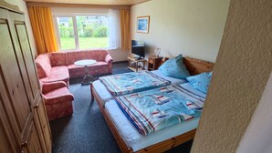 Un dormitorio con cama, sofá, televisión y ventana con cortinas.