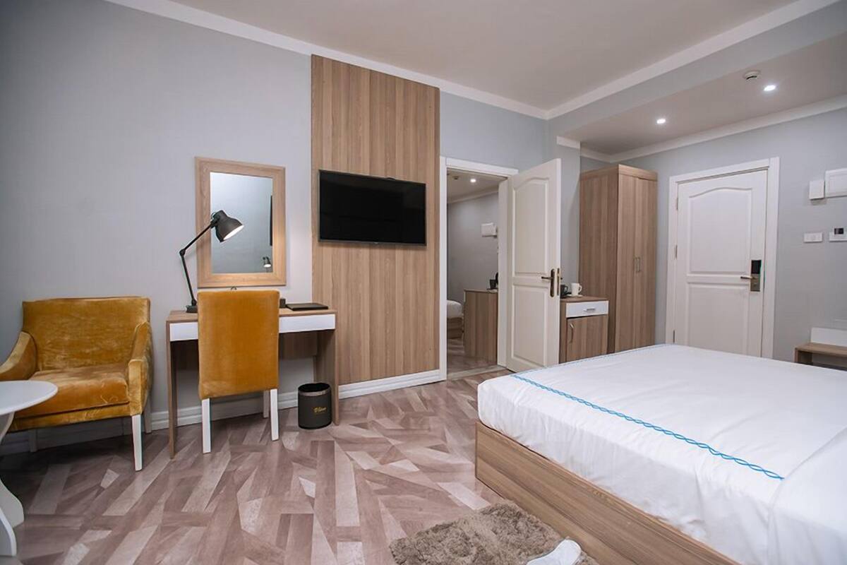 A modern hotel room with a bed, a desk with a chair, a TV, and a wardrobe.