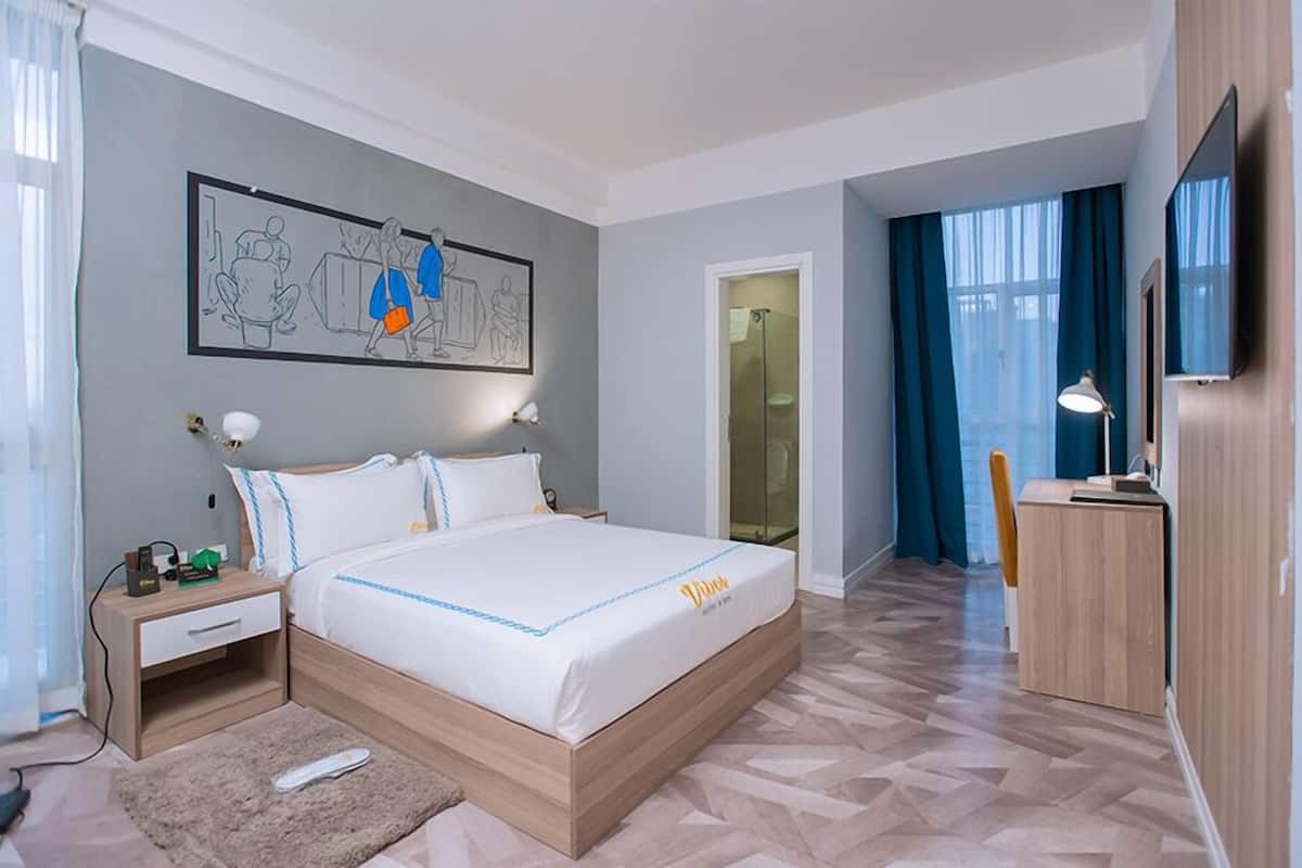 A hotel room with a bed, bedside table, lamp, and a desk with a chair.