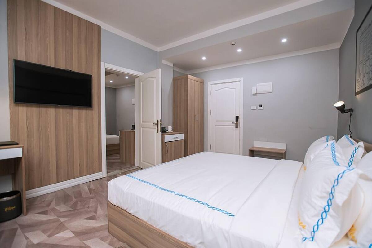 A bedroom with a bed, a TV mounted on the wall, a wardrobe, and a desk with a chair.