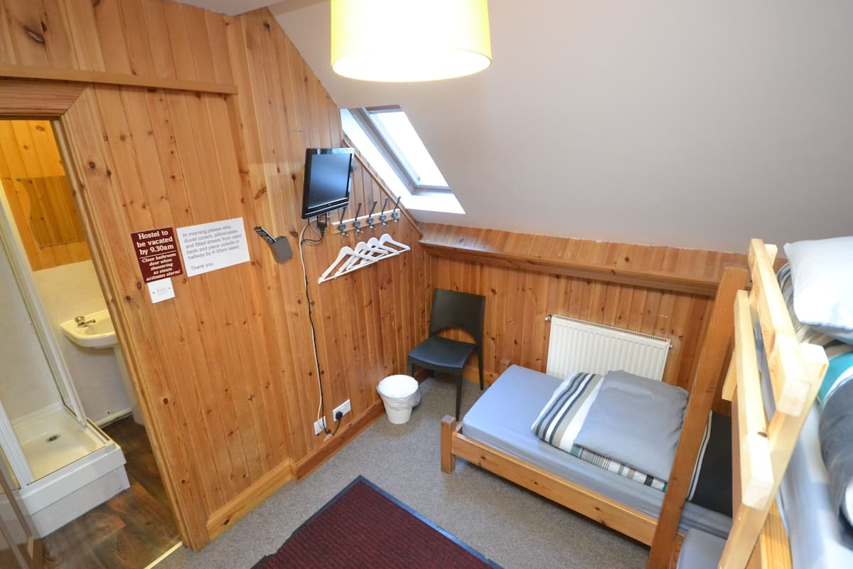 Una habitación de madera con cama, una silla, una mesita, un televisor, una ventana y un letrero.