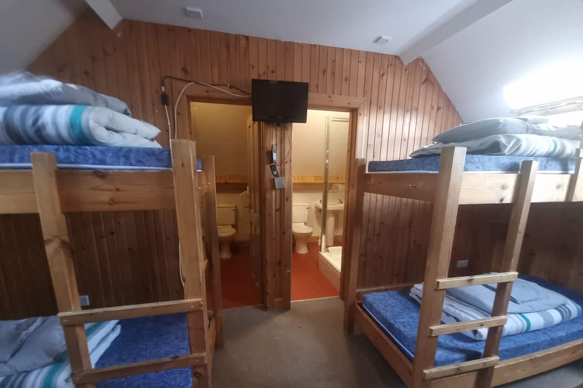 Habitación tipo dormitorio con literas, paredes de madera, un televisor y un baño visible a través de una puerta abierta.