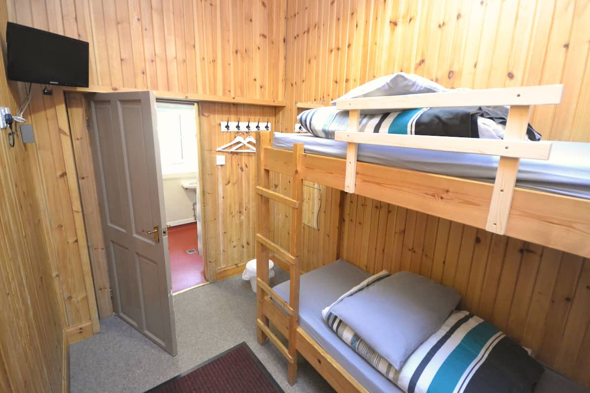 Habitación con literas de madera y un televisor montado sobre la cama.